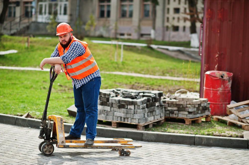 The image shows a construction worker or laborer operating a pallet truck at a construction site.
